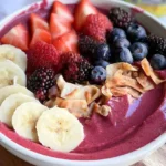 Thick smoothie bowl topped with sliced bananas, fresh berries, chia seeds, and crunchy granola.