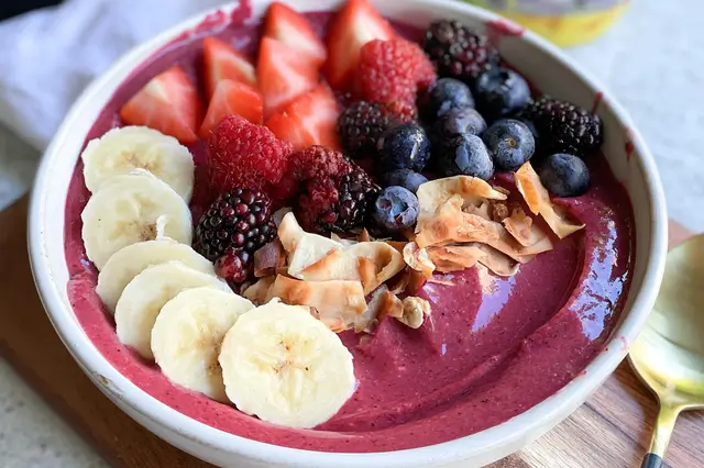 Thick smoothie bowl topped with sliced bananas, fresh berries, chia seeds, and crunchy granola.