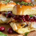 Turkey cranberry sliders topped with melted cheese and cranberry sauce on mini brioche buns.