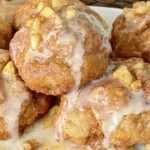 Baked Apple Fritters: A Delicious and Easy Recipe 5 Warm baked apple fritter drizzled with sweet powdered sugar glaze on parchment paper.