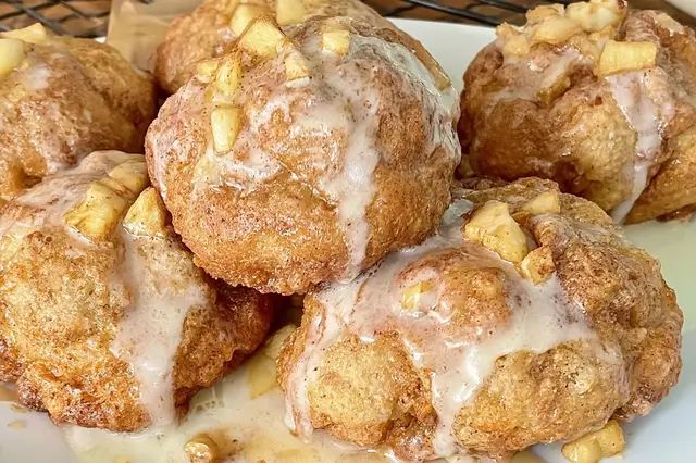 Baked Apple Fritters: A Delicious and Easy Recipe 3 Warm baked apple fritter drizzled with sweet powdered sugar glaze on parchment paper.