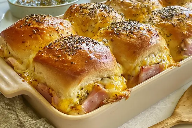 Baked ham and cheese sliders topped with melted butter, poppy seeds, and dried minced onion