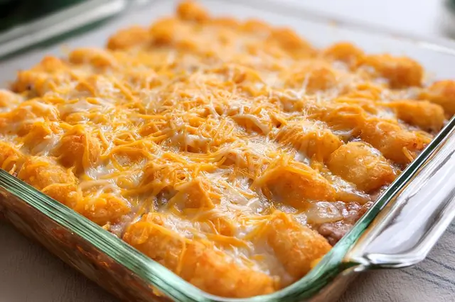 Baked ground beef tater tot casserole with melted cheddar cheese in a baking dish.